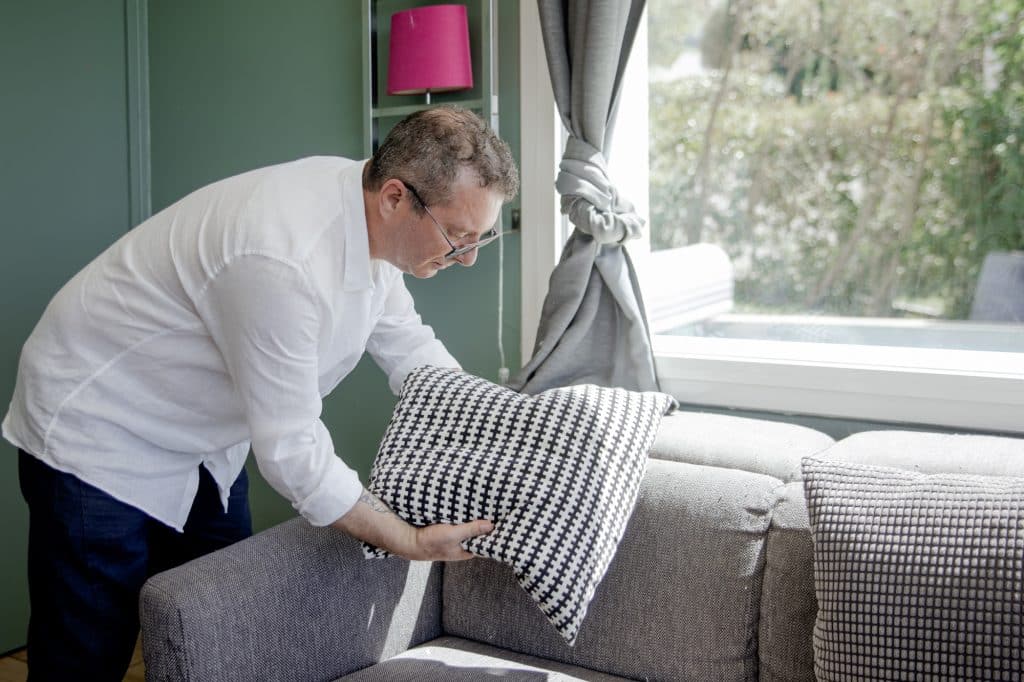Alexandre Dutel Immo5k by efficity votre agent immobilier de confiance qui remet en place un coussin sur un canapé d'une maison à vendre avant une visite
